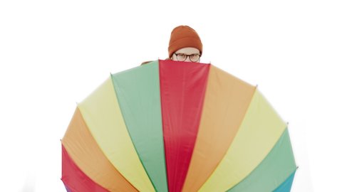 Charming Caucasian man shows multicoloured umbrella to the camera and spins it white background isolated copy space studio shot . High quality 4k footage