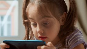 Close-up shot of a little girl while using a smartphone at home. Concept: the future of web technologies, video technologies, connections and visions of the future of children with the Internet.