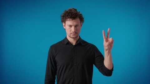 Upset tired man showing two finger peace sign gesture unhappy sad posing isolated on blue studio male depressed worry for distress anxiety frustrated trouble pain face expression irony and sarcasm