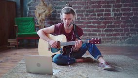 Man acoustic guitar sitting floor with laptop and headphones playing singing song online music lessons. Caucasian young guitar player practicing musical instrument video call Serenade for girlfriend