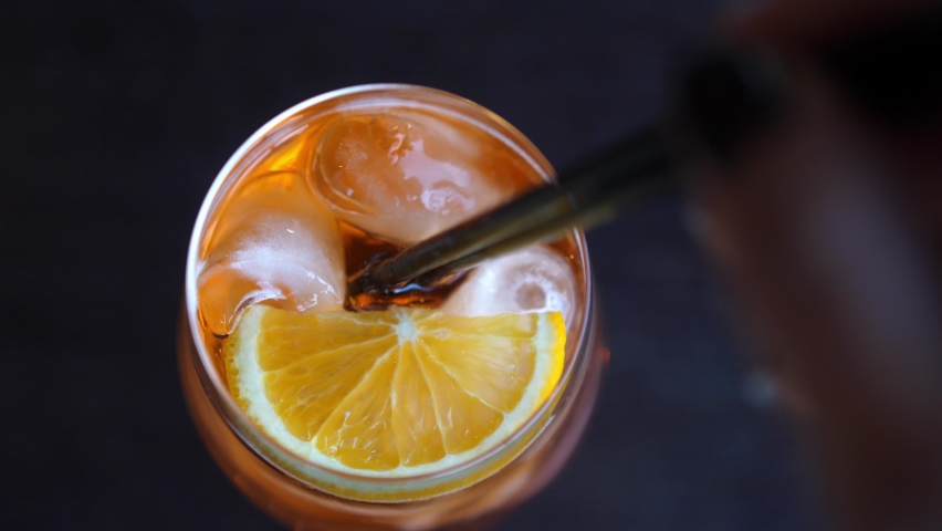 Hand mixes an orange drink cocktail with black cocktail tube. Glass of orange soda with ice. Top of view Royalty-Free Stock Footage #1088686857