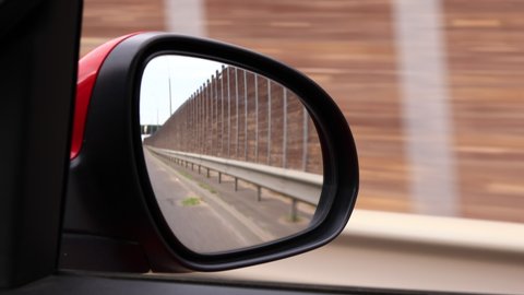 View in the rear view side mirror of a auto, driving a red car along the track