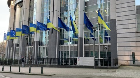 Brussels, Belgium - March 2, 2022: EU and Ukrainian flags are waving in from of the European Parliament building. Flags were raised to show the support for Ukraine against Russian aggression