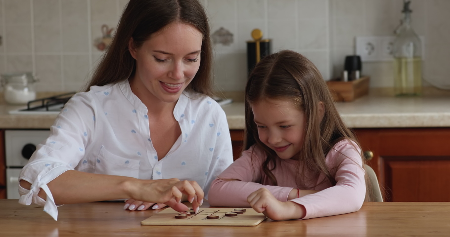 Adorable little girl and mother playing checkers seated at table in kitchen. Woman her cute daughter involved in interesting wooden boardgame, develop strategic skills enjoy playtime together at home Royalty-Free Stock Footage #1088688475