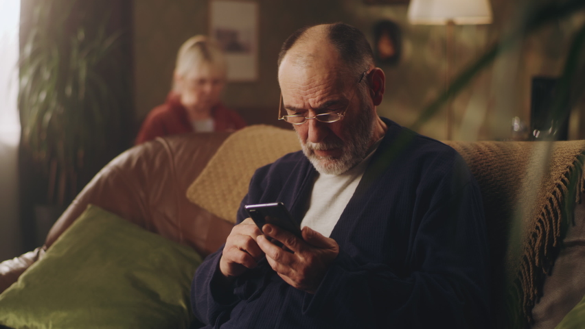 Elderly depressed man on sofa taking off glasses while holding phone with bad news and worried Royalty-Free Stock Footage #1088689287