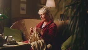 A retired woman knitting a warm sweater at her leisure time while sitting on the sofa in the evening near her husband with newspaper - Powered by Shutterstock - Get 15% off with code: PIKWIZARD15