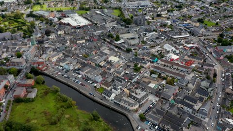 Forwards fly above town. High angle view of centre with buildings and squares. Tilt down focusing on roundabout with sculpture in middle. Ennis, Ireland