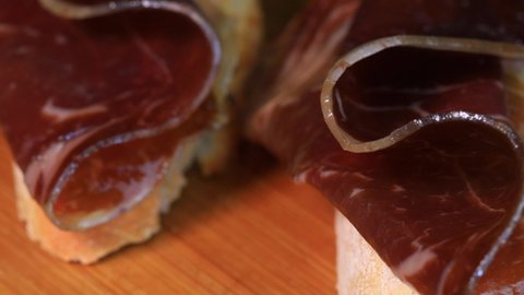 Slices of dried or smoked beef meat on slices o bread, macro shot close up view in 4k. Traditional spanish pinchos rotating on wooden board.