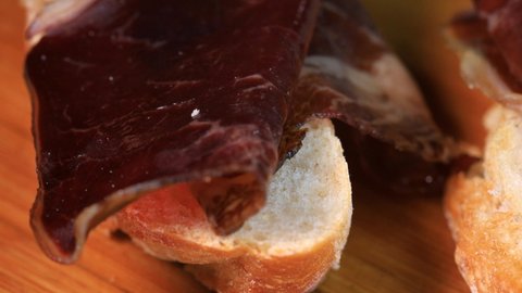 Spanish traditional pincho of beef ham on bread. Rotation motion, close up view macro shot.