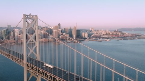Cars driving to San Francisco downtown by the Bay Bridge highway road on clear day in early morning sunrise light. Cinematic aerial panoramic drone footage with San Francisco cityscape view at bay 4K