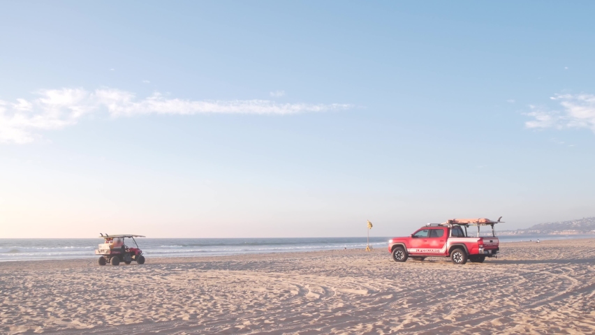 Lifeguard red pickup truck, life guard auto on sand, California ocean beach USA. Rescue pick up car on coast for surfing safety, lifesavers 911 vehicle and sea waves of Mission beach near Los Angeles.