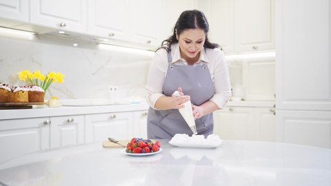 a female chef adds jam from a pastry bag to Anna Pavlova cakes in the kitchen. recipes for delicious traditional desserts. cooking school and courses. Record video and photo lessons.