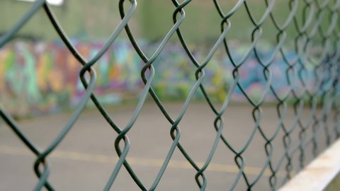 Green chain-link fence on the background of wall graffiti in blur. Close-up