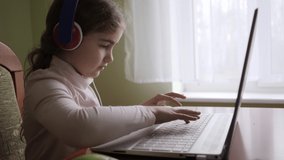 Distance Learning. Schoolgirl Studying Online Using Laptop. School Student Wearing Headphones Watching Internet Course. Future Programmer to Learn Programming. Child Playing on Computer Games.