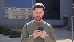 Bearded young smart businessman using smartphone in city. The man holding phone standing outdoor surfing internet social media using new app. Telecommunication and mobile network for business concept. - Powered by Shutterstock - Get 15% off with code: PIKWIZARD15