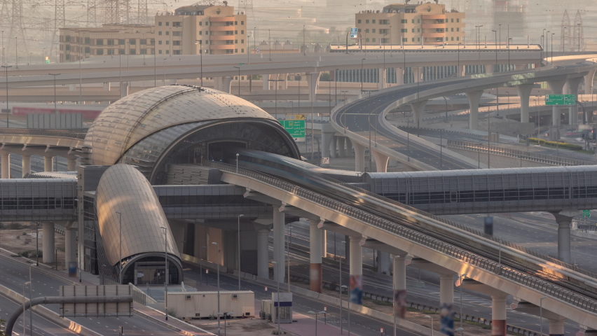 Futuristic building of Dubai metro station and luxury skyscrapers behind in Dubai Marina aerial timelapse. Traffic on Sheikh Zayed road highway junction during sunset, United Arab Emirates