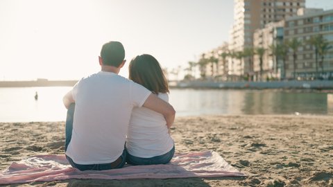 Man and woman couple hugging each other sitting on towel at beach