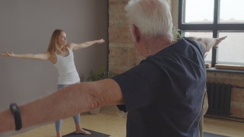 Side view of aged Caucasian man and woman doing exercise in yoga studio with younger female instructor at daytime