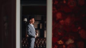 A man puts on a jacket standing in a room. The camera shoots from the side through the doorway. - Powered by Shutterstock - Get 15% off with code: PIKWIZARD15