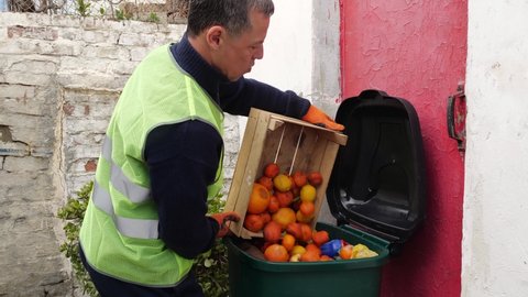 Food Waste in Grocery Store Retail. Supermarket worker throws discarded unsold damaged fruits in the trash