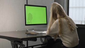 College student watching lesson online and studying from home. Young woman taking notes while looking at computer screen following professor doing math on video call. Green screen