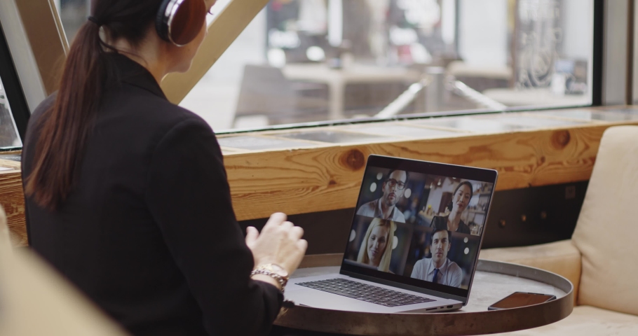 Back view of young caucasian woman with headphones during a meeting conference in a public bar. Attractive businesswoman in smart casual suit having a conference meeting in coffee shop