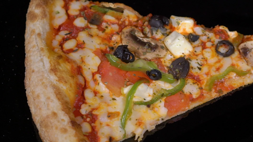 Piece slice of pizza with vegetables and cheese. Olives, pepper and tomato. Food on plate turning on black isolated background. Showcase in restaurant pizzeria.