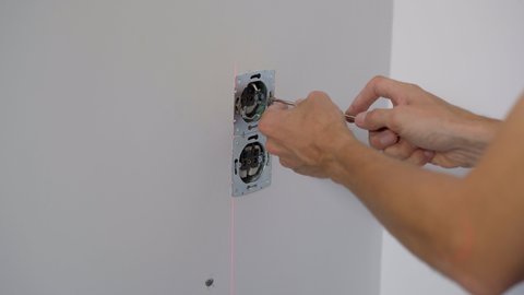 An electrician installs an electric socket outlet into wall. Construction and home repair