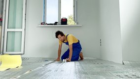 A professional master of underfloor heating installation is laying out and glue the insulation for the floor, on which he will then lay the laminate. Slowmotion video