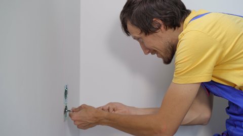 An electrician installs an electric socket outlet into wall. Construction and home repair