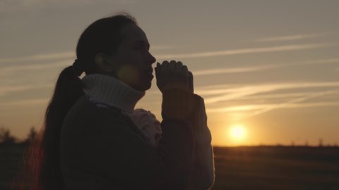 girl praying at sunset in the sky, silhouette of a woman asking for help, reading prayer in sun, living as believer, Ramadan at dawn, getting rid of sins, meditating with palms of her hands together.
