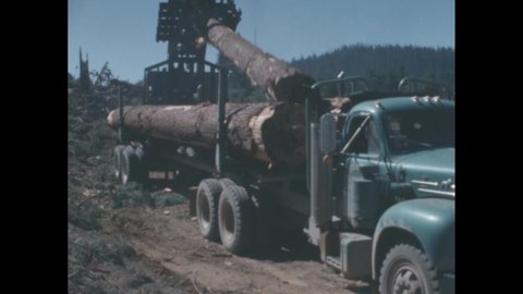 1950s: Crane moving log. Crane sets log in back of truck.
