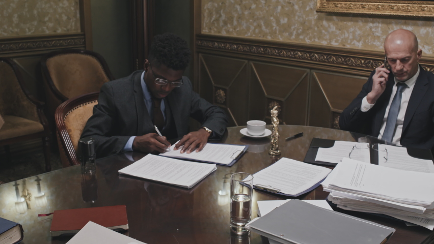 Zoom in shot of African American lawyer in formal suit signing and stamping document while working with colleagues in office Royalty-Free Stock Footage #1088714243