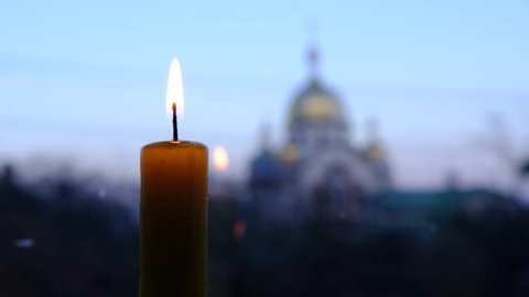 burning candle wit a blured church on background with the stained-glass windows Location: Ukraine.