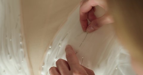 the hands of the seamstress carefully sticks the pins into the corset of the wedding dress on the mannequin. production of a wedding dress. close-up