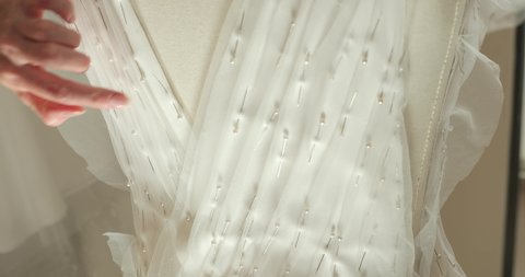 female hands of a seamstress sticks pins into the corset of a wedding dress on a mannequin. production of a wedding dress. close-up