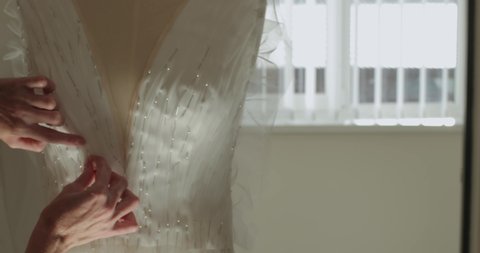 female hands of a seamstress sticks pins into the corset of a wedding dress on a mannequin. production of a wedding dress. against the window. close-up