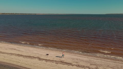 Two people man and woman running by sand beach coastline between water, sand bar at Mykolaiv region, Ukraine. Flying around drone aerial shot