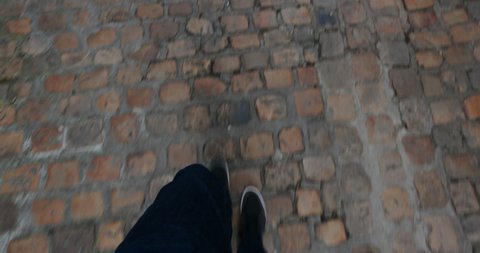 POV look down at man walking on cobbled street wearing blue jeans and trainers