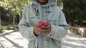 Front view of smiling young african american woman using mobile phone while walking in city park - Youth, social media and millennial people concept. High quality FullHD footage