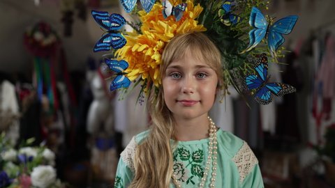 Close-up portrait of charming Ukrainian little girl looking at camera smiling. Beautiful kid in national embroidered dress and head wreath posing in slow motion indoors. Nationality and individuality