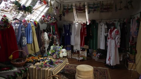 Wide shot room with traditional Ukrainian embroidered dresses and flowers. Authentic national clothes in shop indoors. Culture and individuality concept