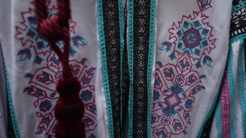 Front view embroidered Ukrainian traditional shirt hanging indoors. Close-up multicolored embroidery on national clothes, tilting shot. Slow motion