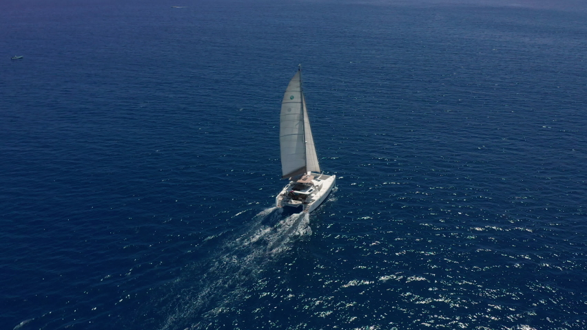 Aerial footage, rear view of luxury sailboat sailing on a deep blue sea with white wakes. Camera follow catamaran in blue ocean water Royalty-Free Stock Footage #1088719531