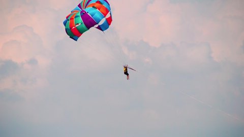 para sailing gliding under colorful parachute canopy hanging with bare legs in harness against a cloudy dusk sky in the windy weather showing adventure water sports in Havelock Andaman Nicobar island