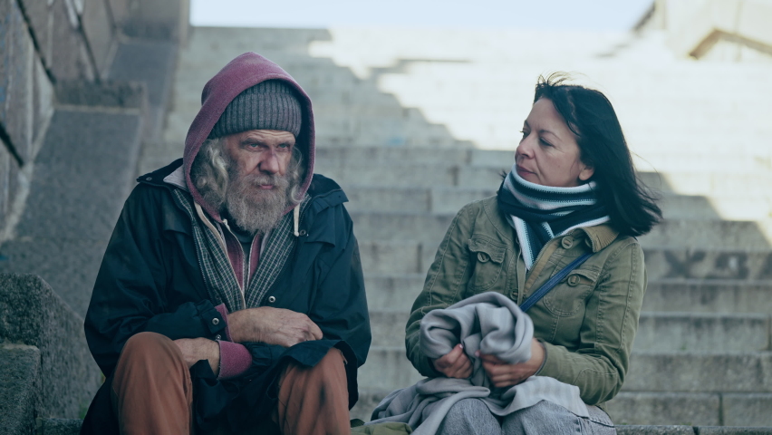 Female social worker wrapping senior homeless man in a blanket, human empathy | Shutterstock HD Video #1088720555