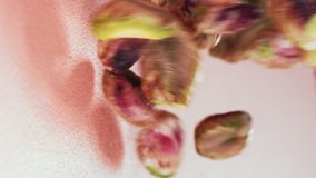 Pistachio dropping on pink background. High angle, close up. Super slow motion 1000fp. Vertical video