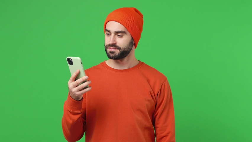 Excited joyful overjoyed happy fun young brunet man 20s years old wears red shirt hat using mobile cell phone hold fan of cash money in dollar banknotes isolated on plain light green background studio Royalty-Free Stock Footage #1088723553