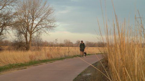 Fort Collins, CO, USA - March 27, 2022: Man is walking with a young dog on a bike trail along the Poudre River in Fort Collins, early spring scenery.