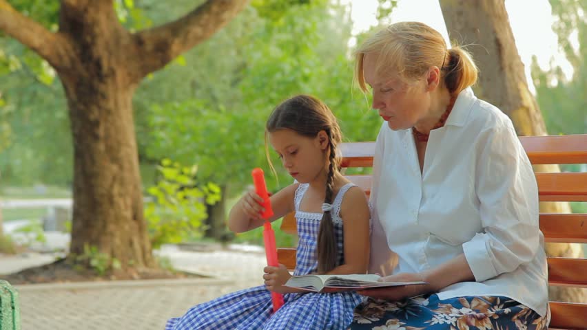 Grandmother and granddaughter spending time on a bench in a green park